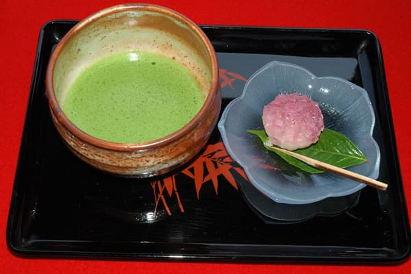 A bowl of Japanese green tea and a rice and bean paste cake with a little stick to eat it with